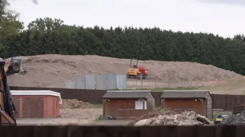 The image shows a tall pile of what looks like dirt with two diggers on top. 