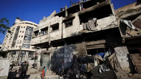 People walk past a ruined building following an Israeli strike in Gaza City