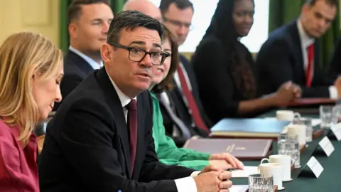 Burham looks up and towards the camera while sitting at a desk surrounded by cabinet members during a cabinet meeting in Downing Street on 21 July.
