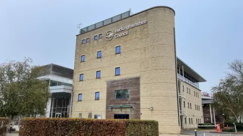 LDRS A view of Buckinghamshire Council's headquarters. The yellow brick building is several stories high and has windows on each floor.