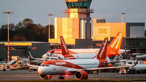 Getty Images Three planes with EasyJet orange and white branding are on the tarmac at Bristol Airport, with the terminal building in the background bathed in the golden light of the setting sun.