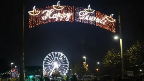 A glittering Happy Diwali sign with a big white ferris wheel in the background