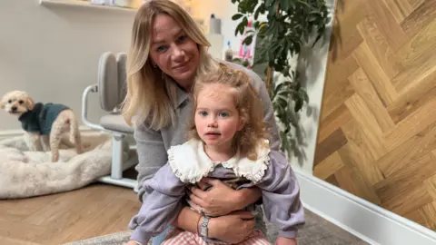Family handout Tilly's sitting in the kitchen at home holding Tilly. 