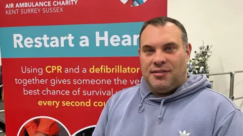 KSS volunteer Steve Harley in Holcombe Grammar School hall beside Restart A Heart banner