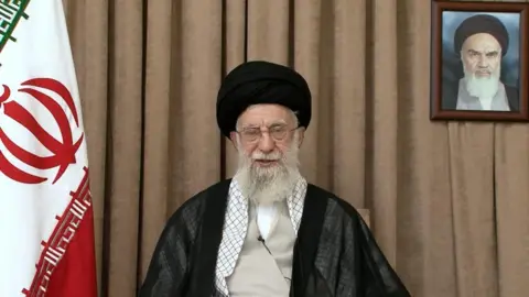 Khamenei addresses the camera, sitting in front of a brown curtain