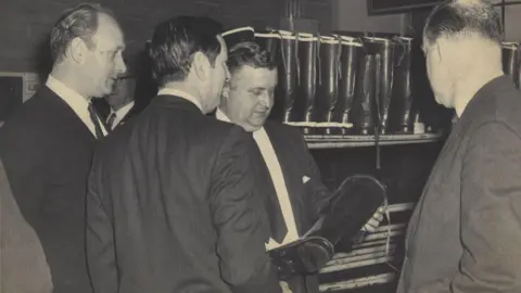 Heritage Service, Dumfries and Galloway Council A group of men in suits and ties examine the quality of a wellington boot