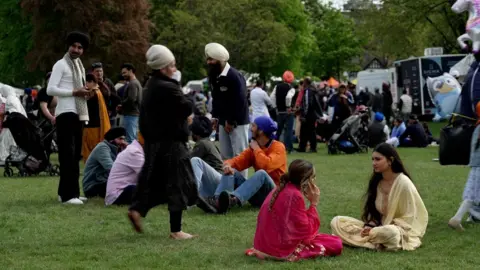 Crowds of people sitting and standing on the grass in a park.