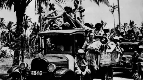 Getty Images A black and white image of defence volunteers in Singapore preparing for an invasion. Groups of men sit in the back of flatbed trucks.