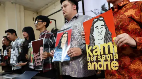 Indonesian activists in line, posing for news photographers while holding posters expressing support of rights activist Andrie Yunus who was injured in an acid attack