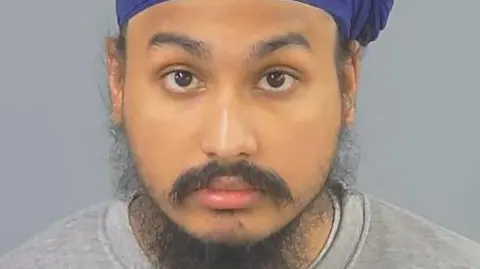 Custody photo of Vickrum Digwa, a man with a beard, a grey jumper and a purple turban looking to the camera.