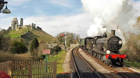 Andrew MP Wright A black steam locomotive travelling past the ruins of Corfe Castle