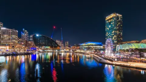 Getty Images The city of Sydney at night, with buildings lit up and the water at Darling Harbour glistening 