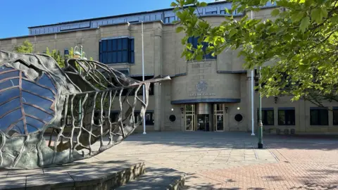 Bradford Crown Court, seen from the outside. A leaf sculpture is in the foreground, with the building seen behind. 
