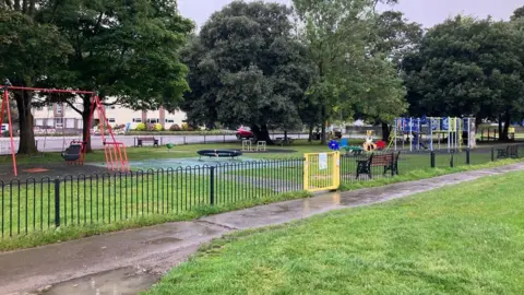 North Somerset Council An empty park with colourful swings and a black metal fence with a yellow gate