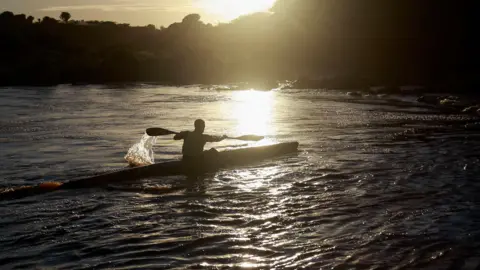 Rogan Ward/Reuters A silhouette of a paddler steering their canoe down a river as the sun sets behind them in  Ximba, South Africa, 21 February 2025.