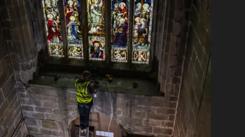 Worker in hi-vis jacked working on stained glass window at St John the Baptist Church