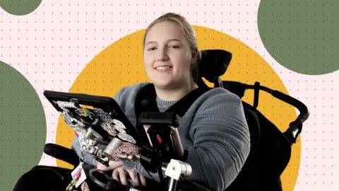 Evie sitting in an electronic wheelchair with a tablet attached is smiling 