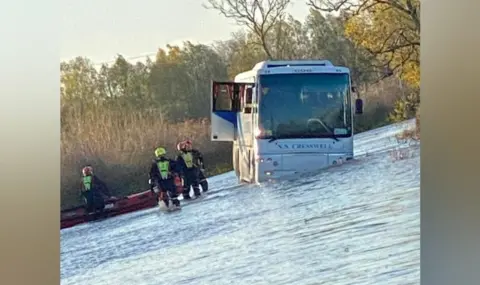 Tor Ward A bus stuck in flood water with a door open. On the left of the photo, near the bus, are at least three firefighters and a small boat. 