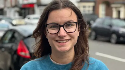 Leah Elston-Thompson Leah in Eccleshall High Street. She wears glasses and a blue jumper.