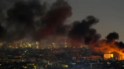 Reuters Smoke rises across the skyline of southern Beirut, appearing to come from a building glowing orange on the far right of the scene.