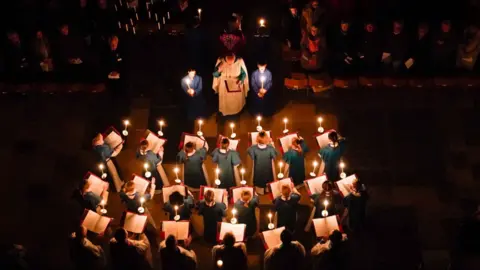 PA Media An aerial shot from high in Salisbury Cathedral looking down in darkness at a choir with each singer holding a lighted candle, looking out towards the congregation.