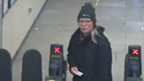 West Mercia Police A slightly grainy CCTV image of Christine Fish walking through train station barriers, with what looks like a ticket in her hand. She is wearing a black outdoor coat, a black hat, and has shoulder-length grey hair and glasses. 