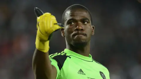 Gallo Images / Getty Images Senzo Meyiwa, in green kit and making a thumbs-up sign with his right hand, on 2 November 2013 during a match in South Africa