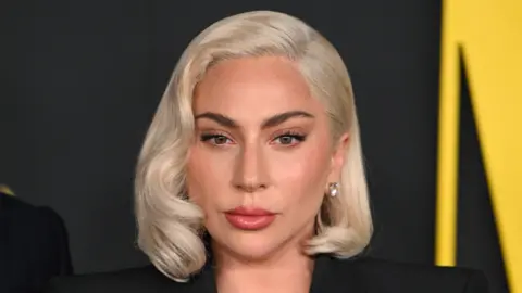 Getty Images Lady Gaga looking at screen, wearing red lipstick and standing in front of black background.