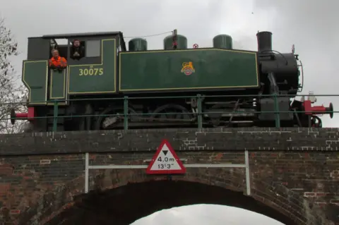 North Dorset Railway A green and black steam locomotive on top of a brick arch railway bridge