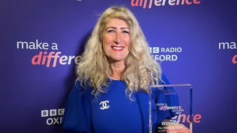 Anna Gatrell stood in front of a purple make a difference background holding an award