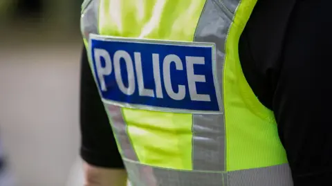 A police officer wearing a hi-vis vert, photographed from behind. You can only see their torso.