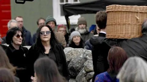 Shows Enya and other mourners at the funeral