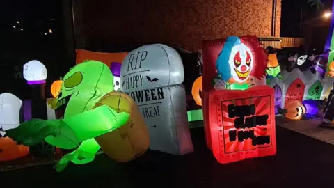A front drive covered with inflatable Halloween figures including a jack-in-the-box, green skeleton, headstone and lots of pumpkins. 