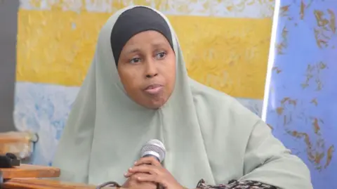 Hodan Mohamud Diiriye in a headscarf holding a microphone and looking to her left.