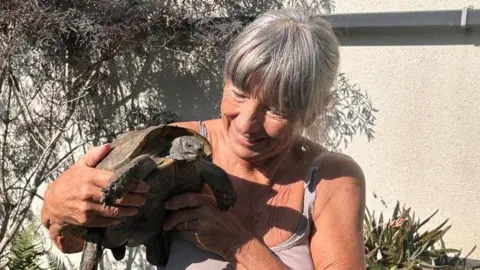 Jacqueline holding her tortoise in her left hand. She is smiling at the tortoise.