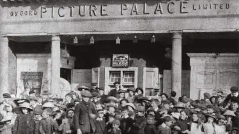 Ultimate Picture Palace An archive photo shows the early days of the Ultimate Picture Palace. A large crowd of people in old-fashioned clothes are gathered out the front of the building. The sign on the building says "Oxford Picture Palace Limited".