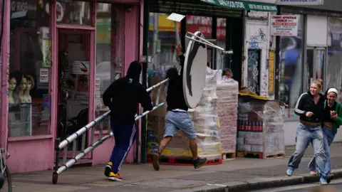 PA A man with a ladder and another with the satellite dish are seen running off down the high street with the Banksy.