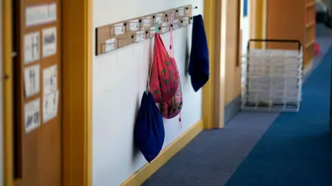 Getty Images The image is of a school corridor which shows a line of pegs with a few bags hanging from them. 