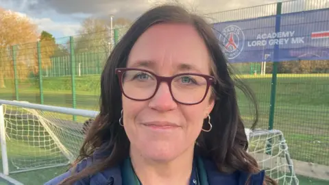 Principal of Lord Grey Academy, Samantha Satyanadhan, standing in front of a small football goal with green metal fencing behind it.