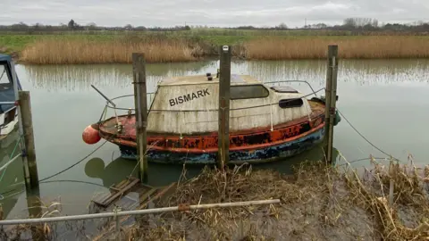 Andrew White An old boat tied up to the riverbank surrounded by overgrown weeds