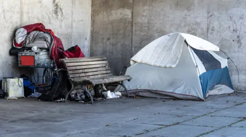 Getty Images A tent and a shopping trolley loaded with possessions beside a park bench.