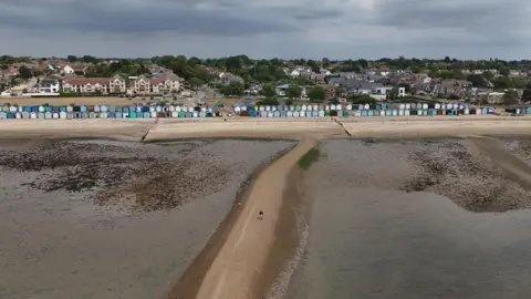 PA Media A drone image showing a long row of beach huts and the sandy beach in front of them. The water has been pictured at low tide. There is a long sandbank that splits the middle of the water.