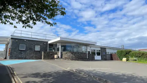 The front of the Ramsey hospital, which is a single-storey stone clad building with a revolving door.