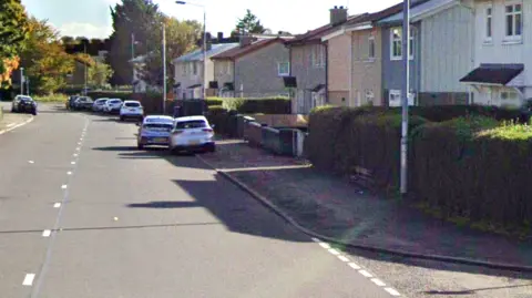 A sunny street of small white houses and some cars