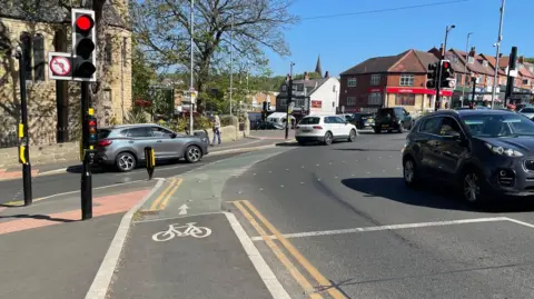New cycle lane and pedestrian crossings at Meanwood Road in Leeds. A traffic light is on red and a car is pulling out of the remodelled junction.
