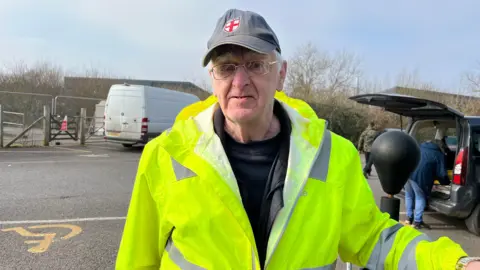 A man stood in a high visibility jacket looking at the camera, wearing a hat with an England flag