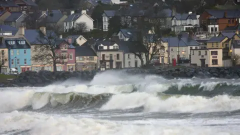 Getty Images In the foreground, large waves. In the background, a row of houses.