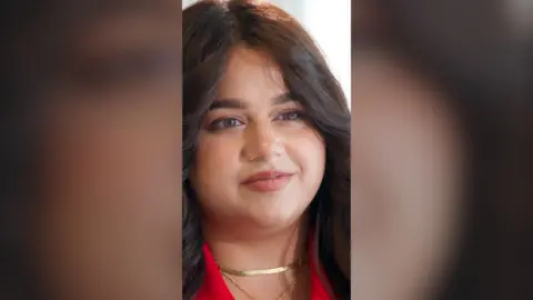 A woman with long brown hair wearing a gold necklace.