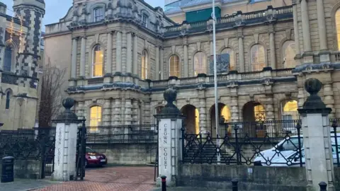 Brian Farmer Reading Crown Court: a brown stone building with lighted windows behind a black metal fence.