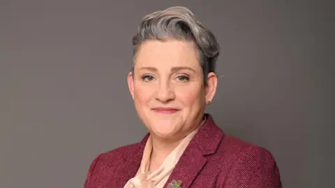UK Parliament Parliamentary portrait of Ashley Dalton. She is wearing a burgundy jacket and a pale pink blouse.